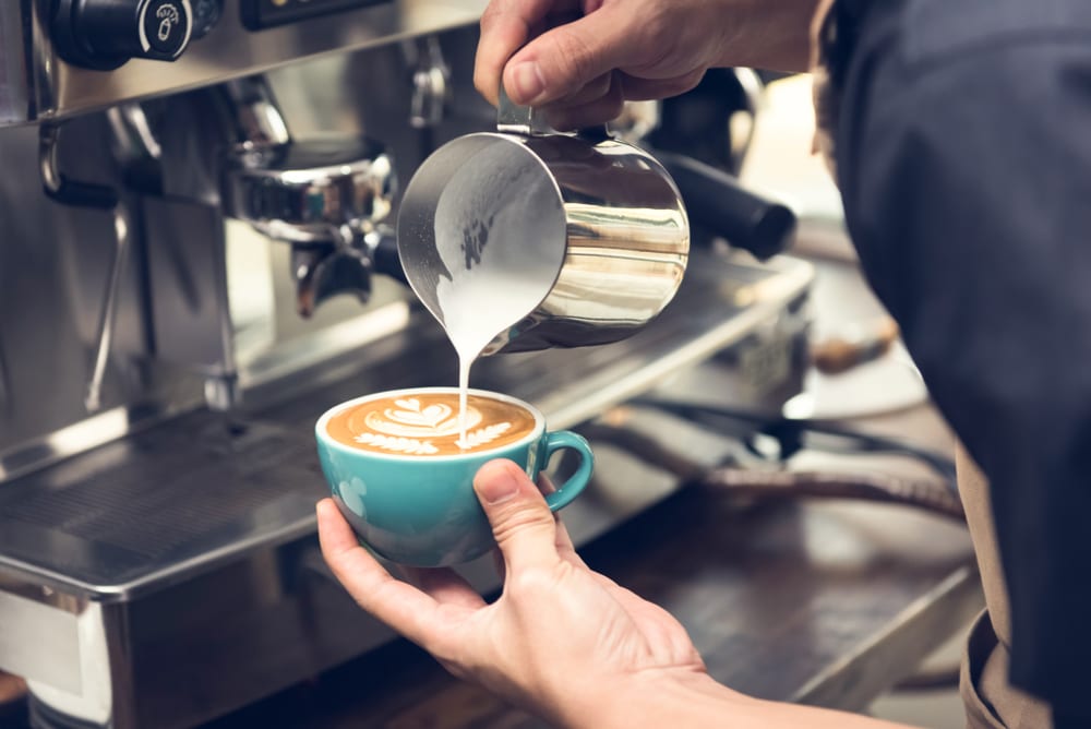 Professional barista pouring steamed milk into coffee cup