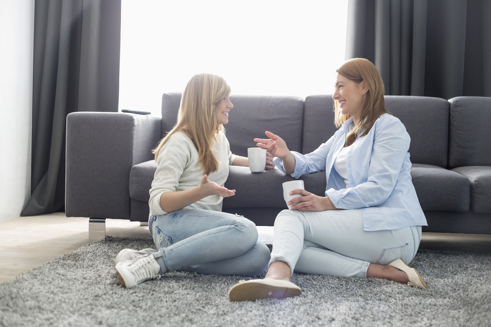 Happy mother and daughter talking while having coffee in living room